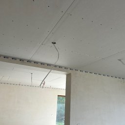 Paweł Petelicki - Montaż płyt gipsowo-kartonowych na suficie z widocznymi przewodami elektrycznymi i fragmentem ściany. Widok na surowy stan wykończenia wnętrza.