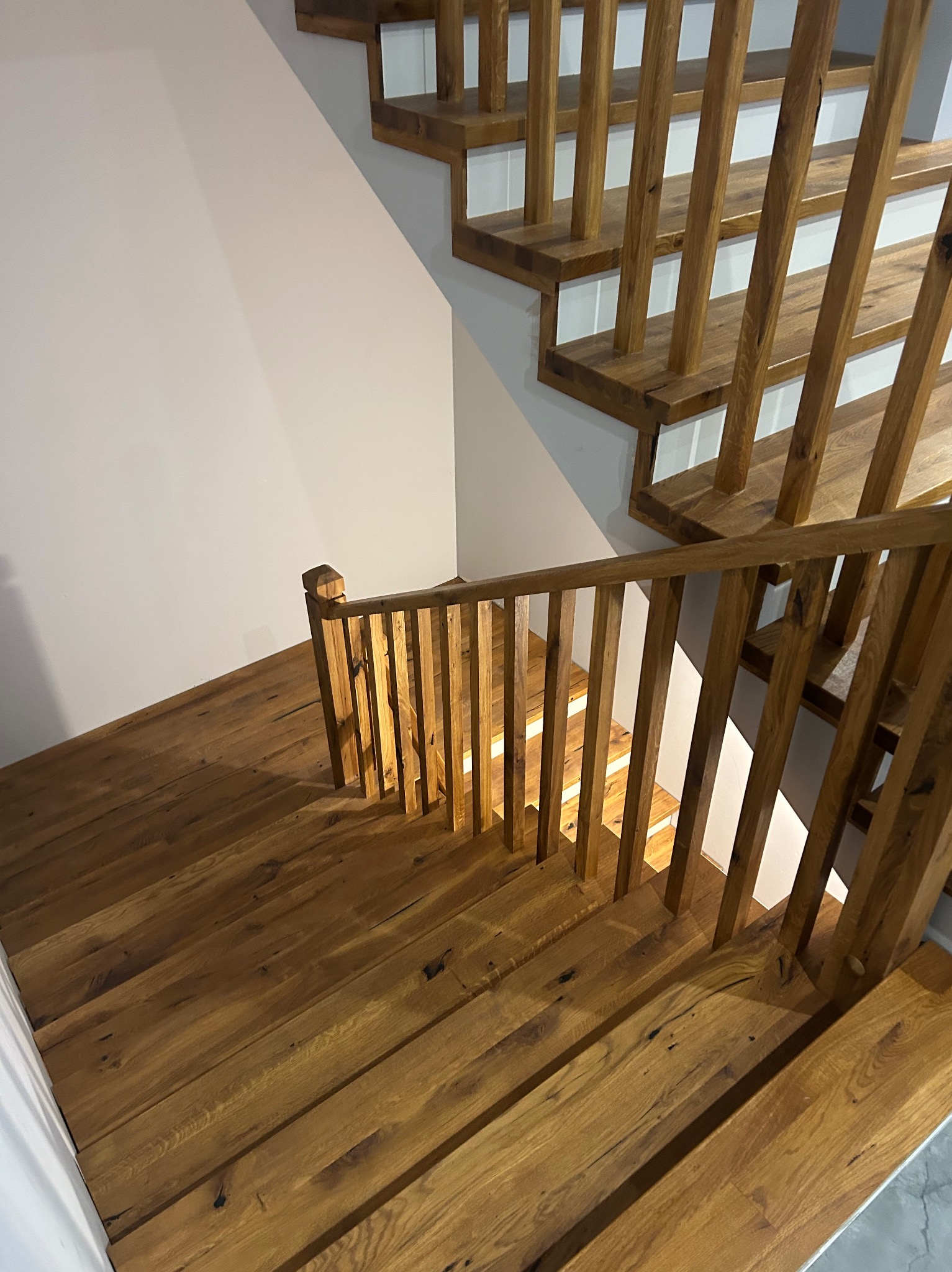 Drewniane schody z balustradą, widok z góry. Naturalne wykończenie drewna, jasne stopnie. Minimalistyczny design, neutralne tło ściany. Detal wykończenia wnętrza.