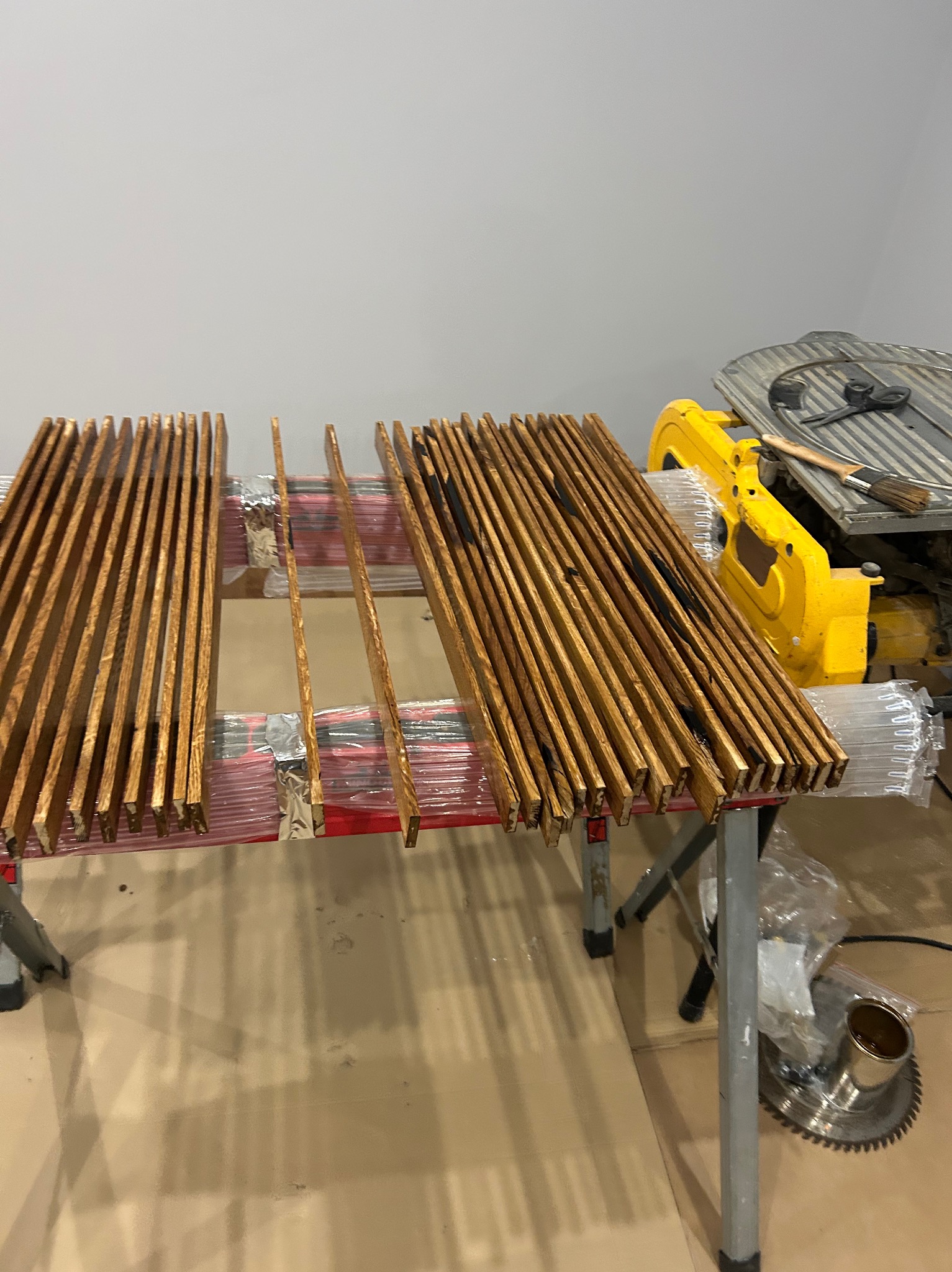 Przygotowane listwy parkietowe na stole roboczym obok piły tarczowej. Elementy drewniane po obróbce, gotowe do montażu. Widoczne narzędzia i akcesoria.