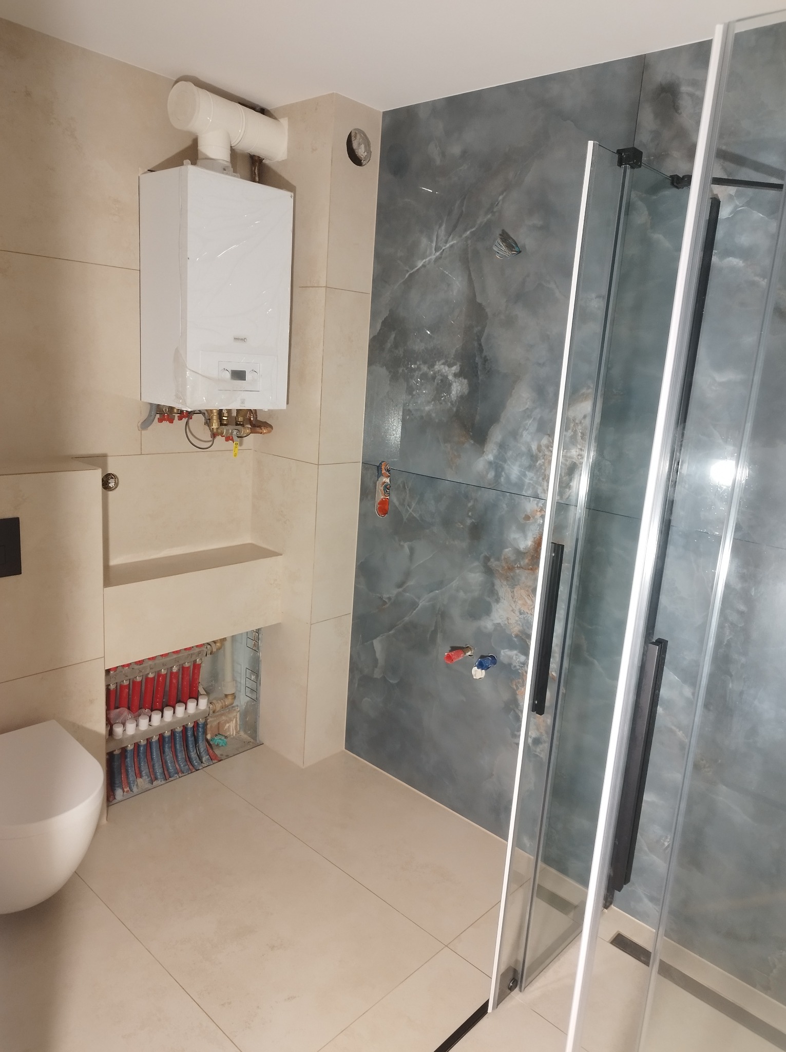 Wykończona łazienka z kabiną prysznicową, piecem gazowym i instalacją podtynkową. Płytki imitujące marmur na ścianie, beżowe płytki podłogowe. Nowoczesny design.