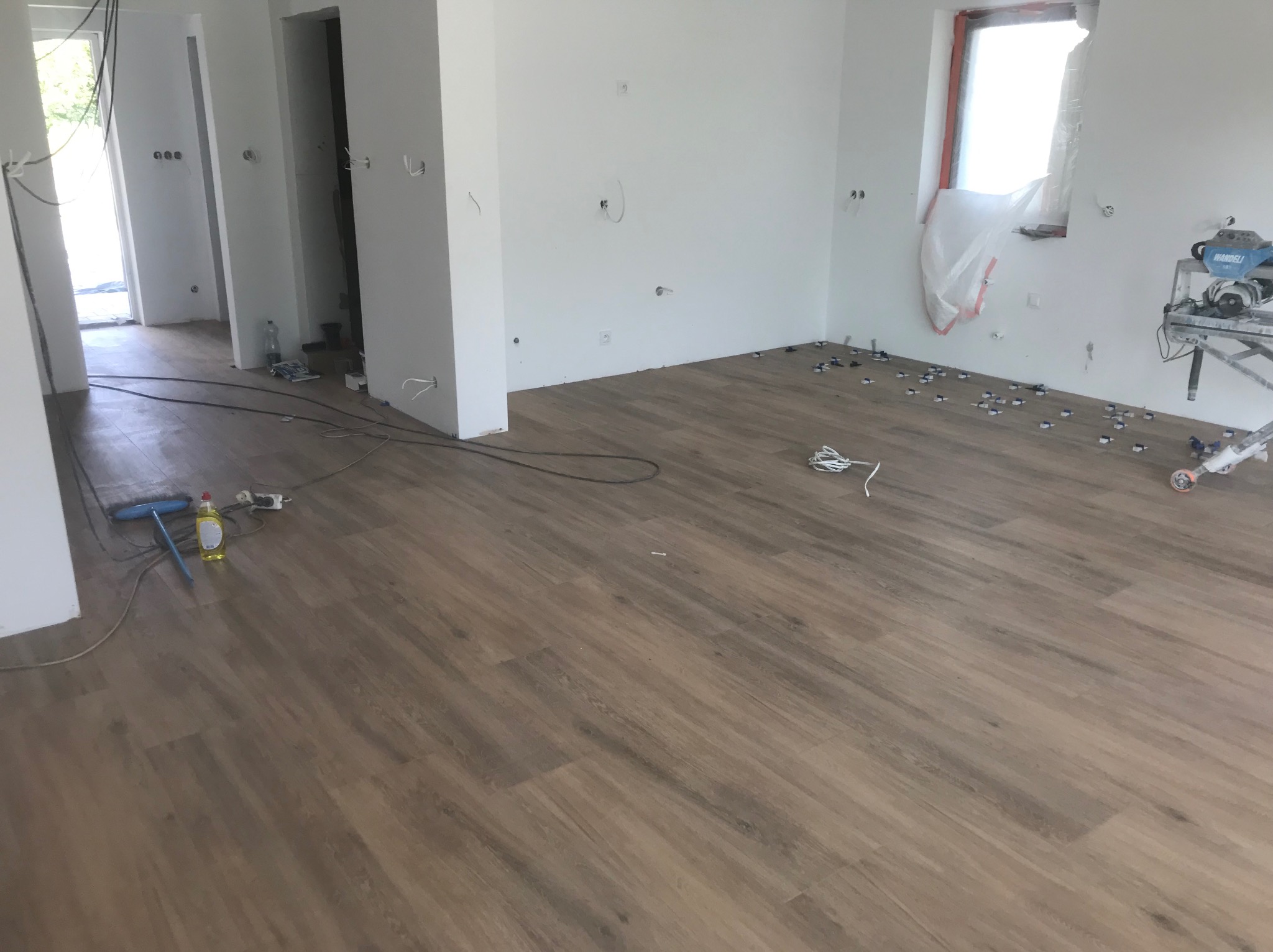 Ułożona podłoga z paneli w jasnym wnętrzu. Widoczne narzędzia i akcesoria do montażu płytek. Przygotowania do dalszych prac wykończeniowych.