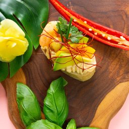 P.H.U KACPER LINKIEWICZ - Apetyczna kanapka z krewetką, awokado i chili na drewnianej desce, ozdobiona bazylią, żółtym kwiatem i liściem monstery. Jasnoróżowe tło. Elegancka kompozycja.