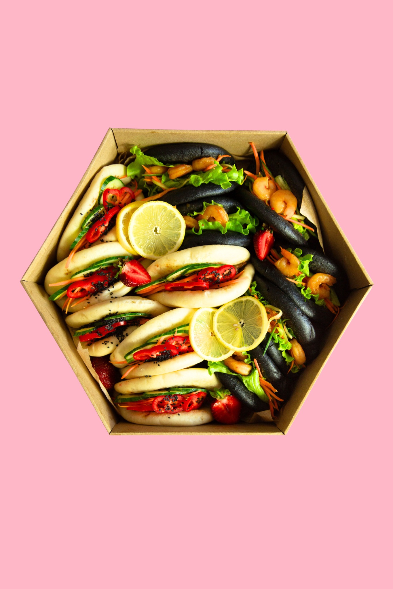 Heksagonalne pudełko z jasnymi i czarnymi bao buns z krewetkami, warzywami i truskawkami na różowym tle. Kreatywna prezentacja dań.