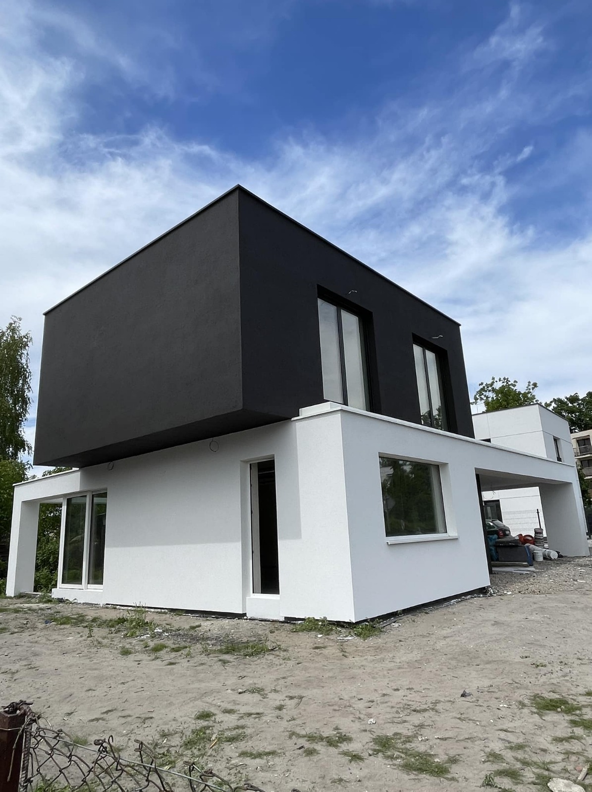 Dwukondygnacyjny dom z czarno-białą elewacją w stylu nowoczesnym. Widoczne okna i fragment otoczenia. Ujęcie z dołu podkreśla bryłę budynku.