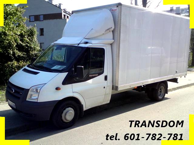 Biały samochód dostawczy Ford Transit z nadbudową kontenerową, zaparkowany na ulicy, z widocznym logo firmy 'TRANSDOM' i numerem telefonu w prawym dolnym rogu zdjęcia.