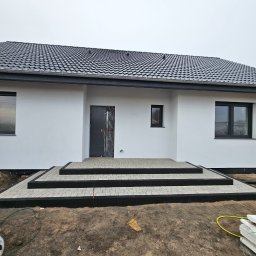 KL-Bruk - Nowoczesny dom z jasną elewacją i schodami wejściowymi wyłożonymi kostką brukową w odcieniach szarości i czerni. Minimalistyczny design, surowy krajobraz.