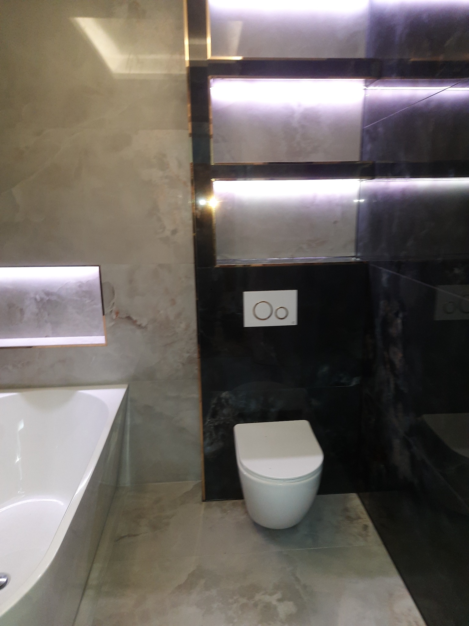 Nowoczesna łazienka z marmurowymi płytkami, podświetlanymi niszami i wiszącą toaletą. Minimalistyczny design z akcentami światła.