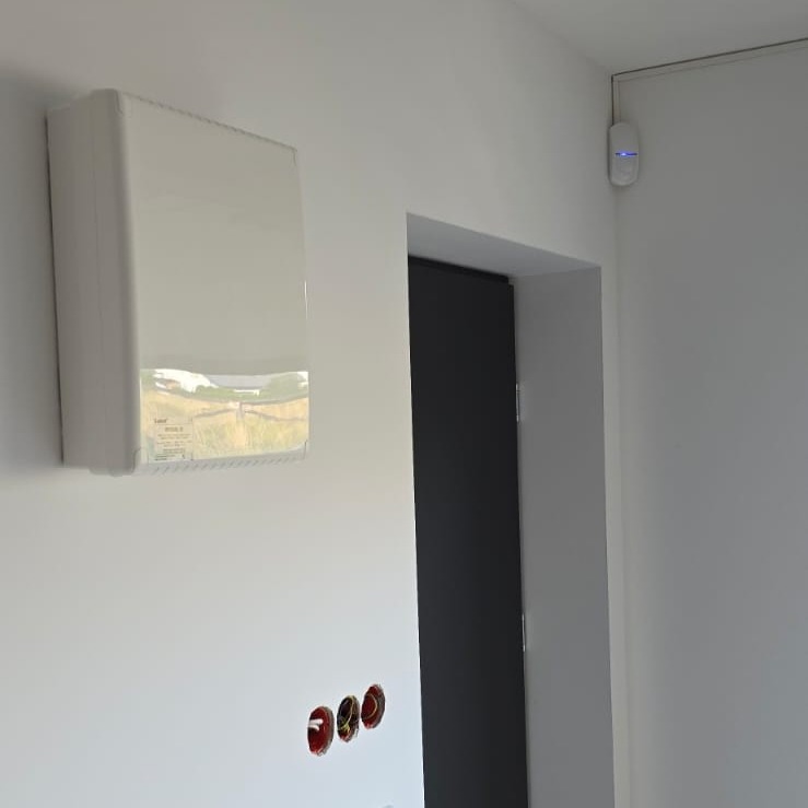 Centrala alarmowa i czujnik ruchu w Uhercach Mineralnych. Widoczne gniazda elektryczne. Minimalistyczny design, białe ściany, nowoczesne rozwiązania.