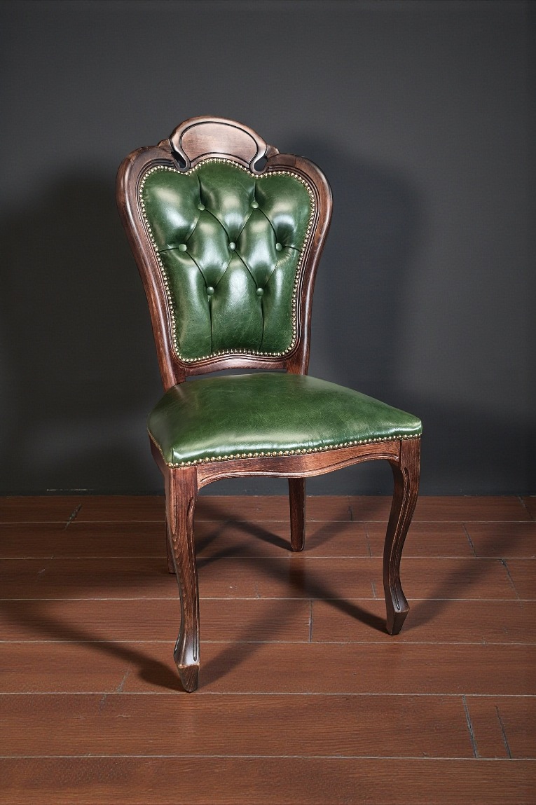 Stylowe krzesło z ciemnego drewna i zieloną, pikowaną skórą, ozdobione złotymi nitami. Elegancki mebel na drewnianej podłodze, na tle ciemnej ściany.