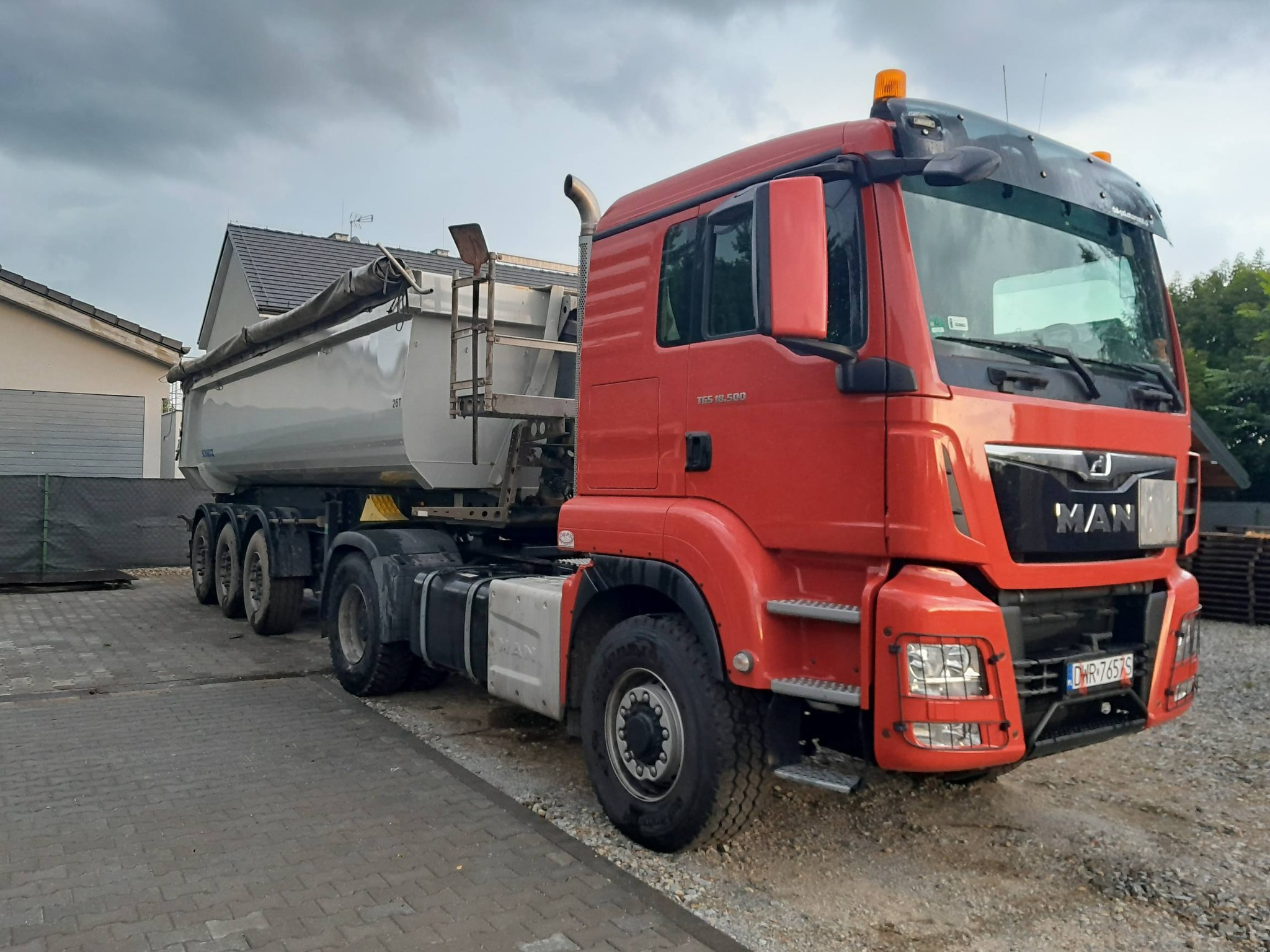 Czerwona ciężarówka MAN z naczepą na kostce brukowej, widok z przodu, pochmurne niebo w tle. Tablica rejestracyjna DWR 7657S.