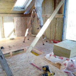 Usługi ogólnobudowlane Dominik kuś - Prace wykończeniowe na poddaszu: ocieplanie wełną mineralną, montaż płyt OSB. Widoczna drabina, narzędzia i okno dachowe. Praca w toku, surowy stan.