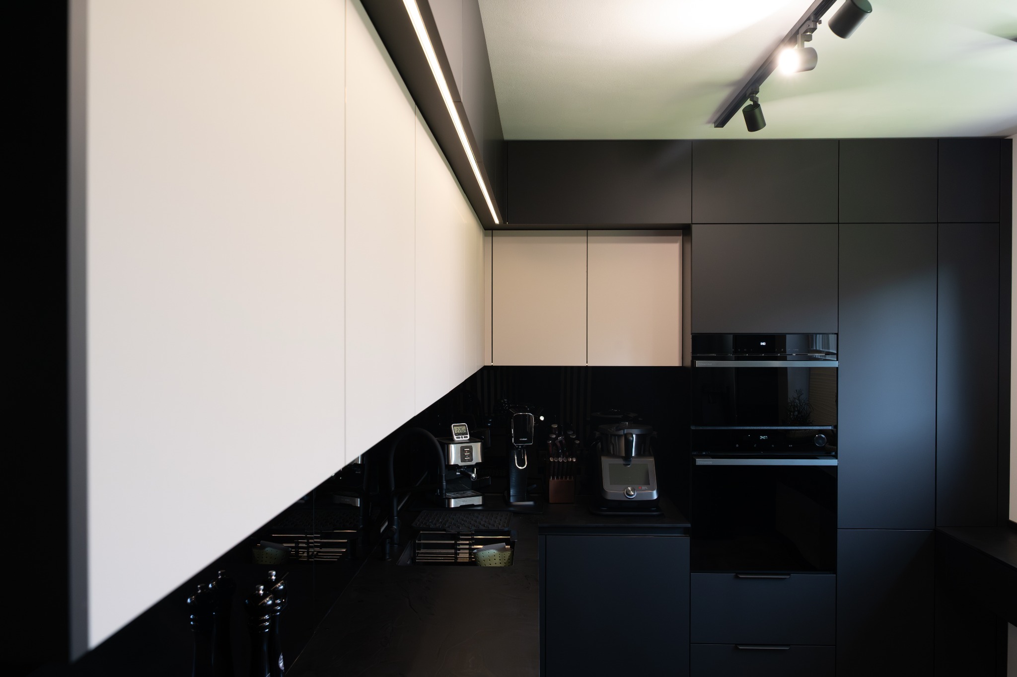 Nowoczesna kuchnia z białymi i czarnymi szafkami, oświetleniem LED podszafkowym i sprzętem AGD. Minimalistyczny design z błyszczącymi powierzchniami.