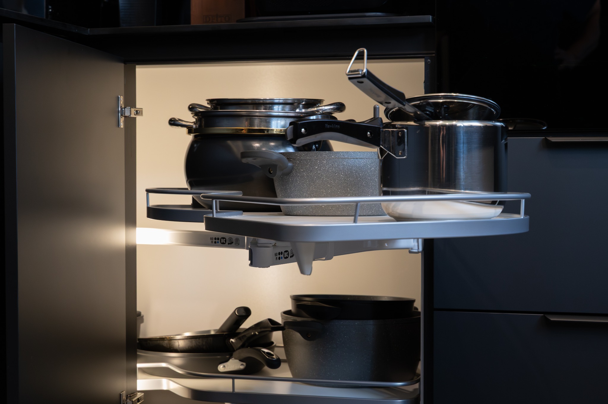 Ciemna kuchnia na wymiar: otwarty narożny słupek z obrotowym systemem przechowywania garnków i patelni. Oświetlenie LED wewnątrz szafki.