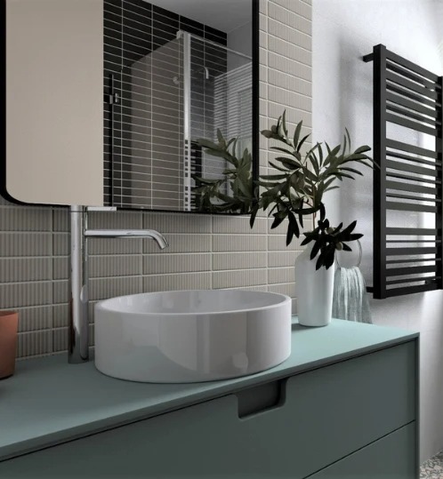 Nowoczesna łazienka z okrągłą umywalką nablatową, chromowaną baterią i grzejnikiem drabinkowym. W tle lustro i płytki w odcieniach szarości. Minimalistyczny design.