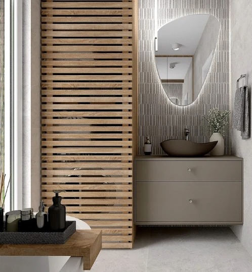 Nowoczesna łazienka z drewnianą przesłoną, asymetrycznym lustrem z podświetleniem LED i minimalistyczną umywalką w odcieniach szarości i brązu.