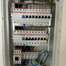 P.U.H. Elektro&CarParts - Rozdzielnica elektryczna z zainstalowanymi bezpiecznikami i przewodami w kolorach: niebieskim, brązowym, zielono-żółtym. Widoczne listwy zaciskowe i aparatura ABB.