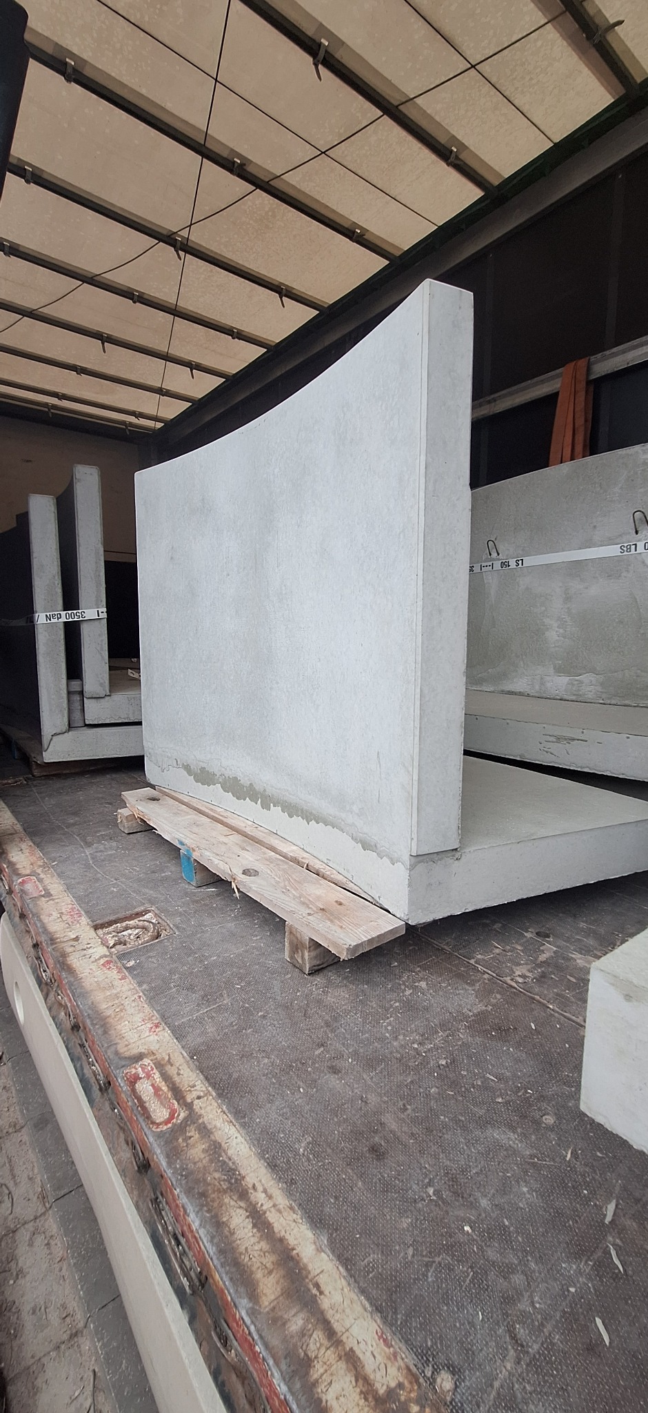 Prefabrykowane elementy betonowe z zaokrąglonym wykończeniem, umieszczone na paletach wewnątrz pojazdu dostawczego, gotowe do transportu na plac budowy.