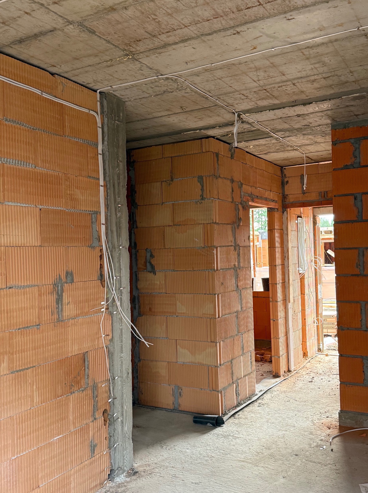 Surowy stan budynku w trakcie prac elektrycznych: widoczne kable prowadzone po ścianach z cegły i pod sufitem, przygotowane do dalszych prac instalacyjnych.