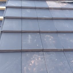 Atom - Ułożona dachówka ceramiczna w kolorze grafitowym z oknem dachowym. Widoczne drewniane elementy konstrukcji dachu. Ujęcie z dołu, podkreślające regularność wzoru.