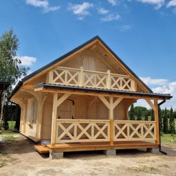 Atom - Drewniany domek letniskowy z balustradą w stylu rustykalnym, widok z zewnątrz w słoneczny dzień. Charakterystyczne zdobienia balustrady i wykończenie dachu.