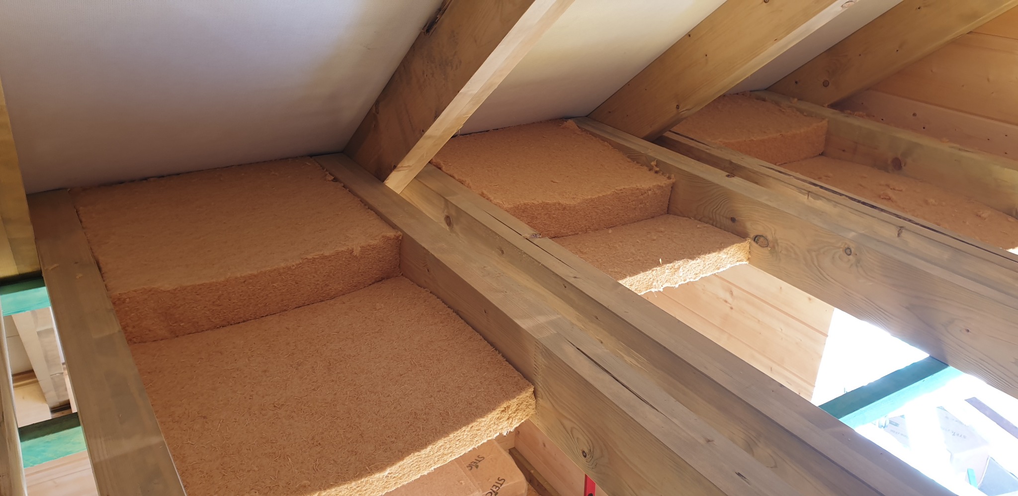 Ocieplenie poddasza wełną drzewną w konstrukcji drewnianej w Bystrej. Widoczne belki i izolacja w przestrzeniach między nimi.
