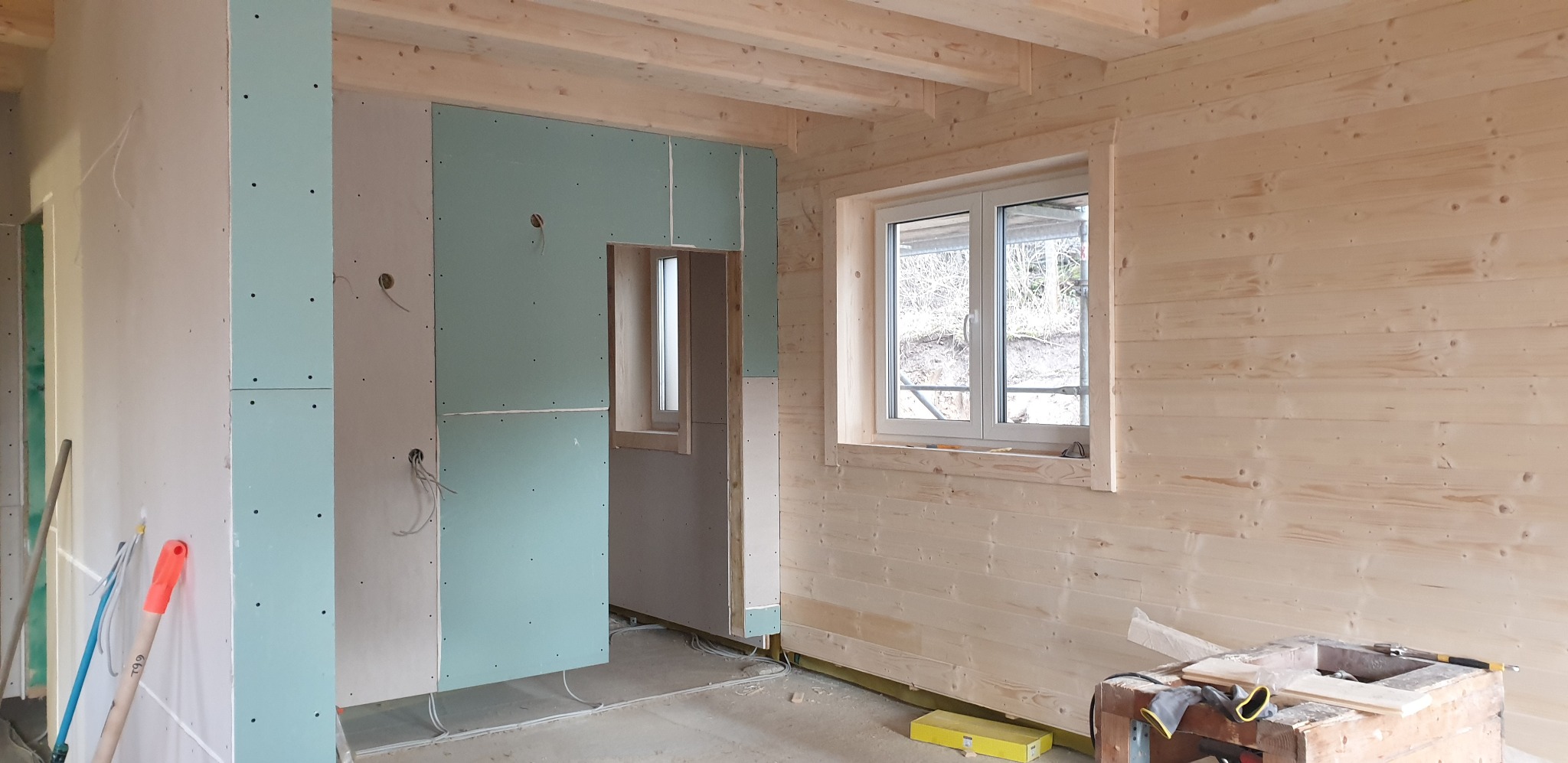 Wnętrze domu w trakcie wykańczania: drewniane ściany, zamontowane płyty karton-gips, widoczne instalacje elektryczne i narzędzia. Etap prac wykończeniowych.