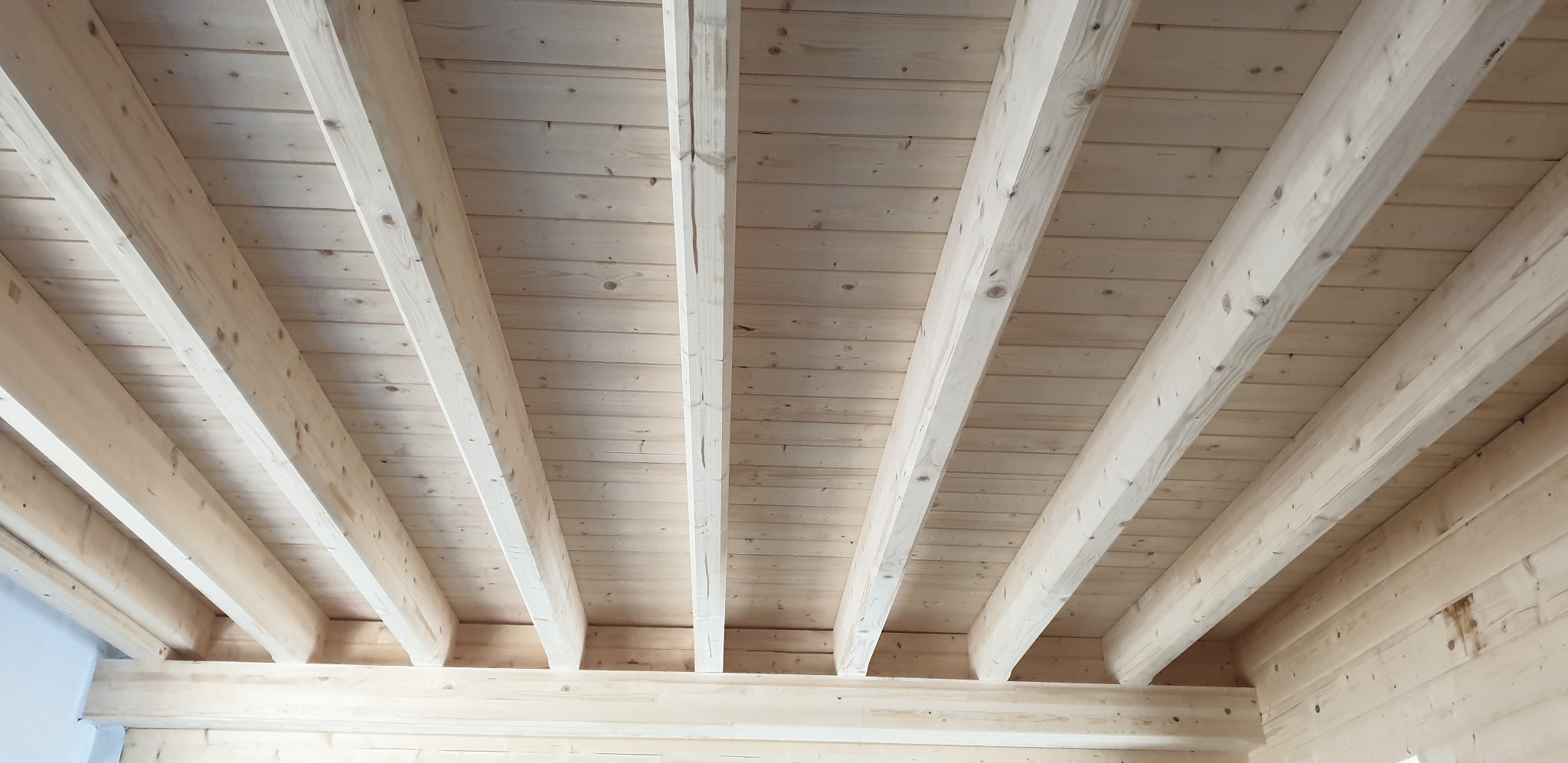 Surowy drewniany strop z belek w jasnym odcieniu, widoczny od dołu, w trakcie budowy domu szkieletowego. Naturalne drewno z widocznymi słojami.
