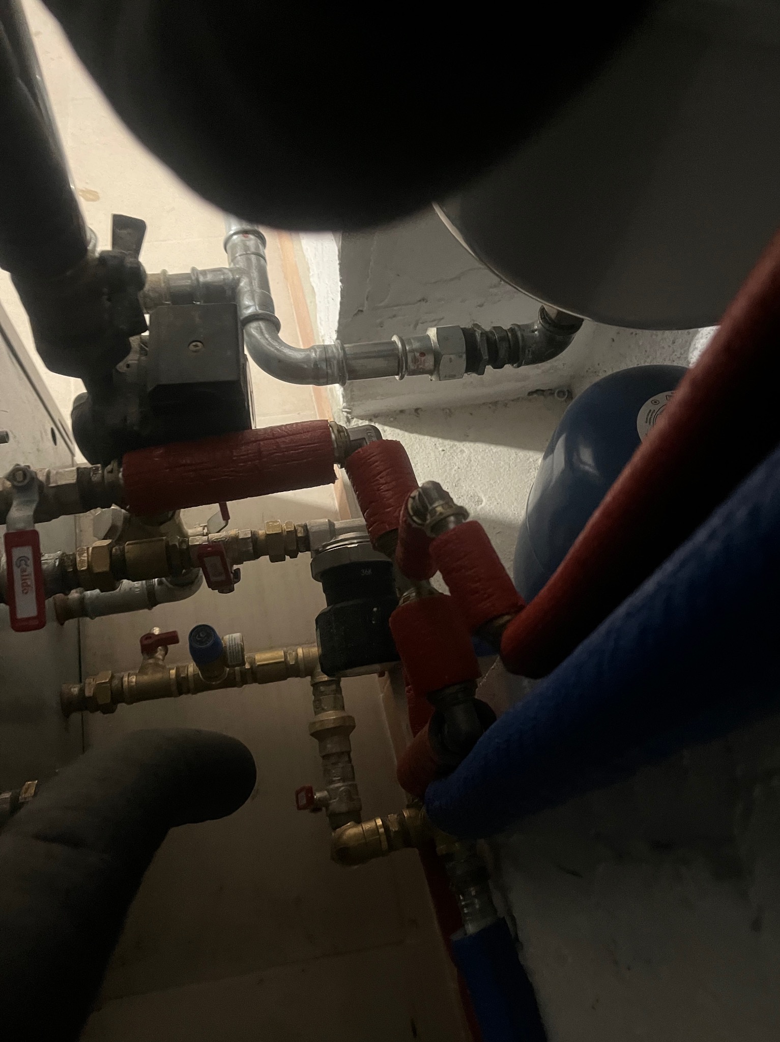 Złożony układ rur miedzianych i zaworów z elementami izolacji termicznej w kolorze czerwonym i niebieskim, tworzący instalację hydrauliczną przy ścianie.