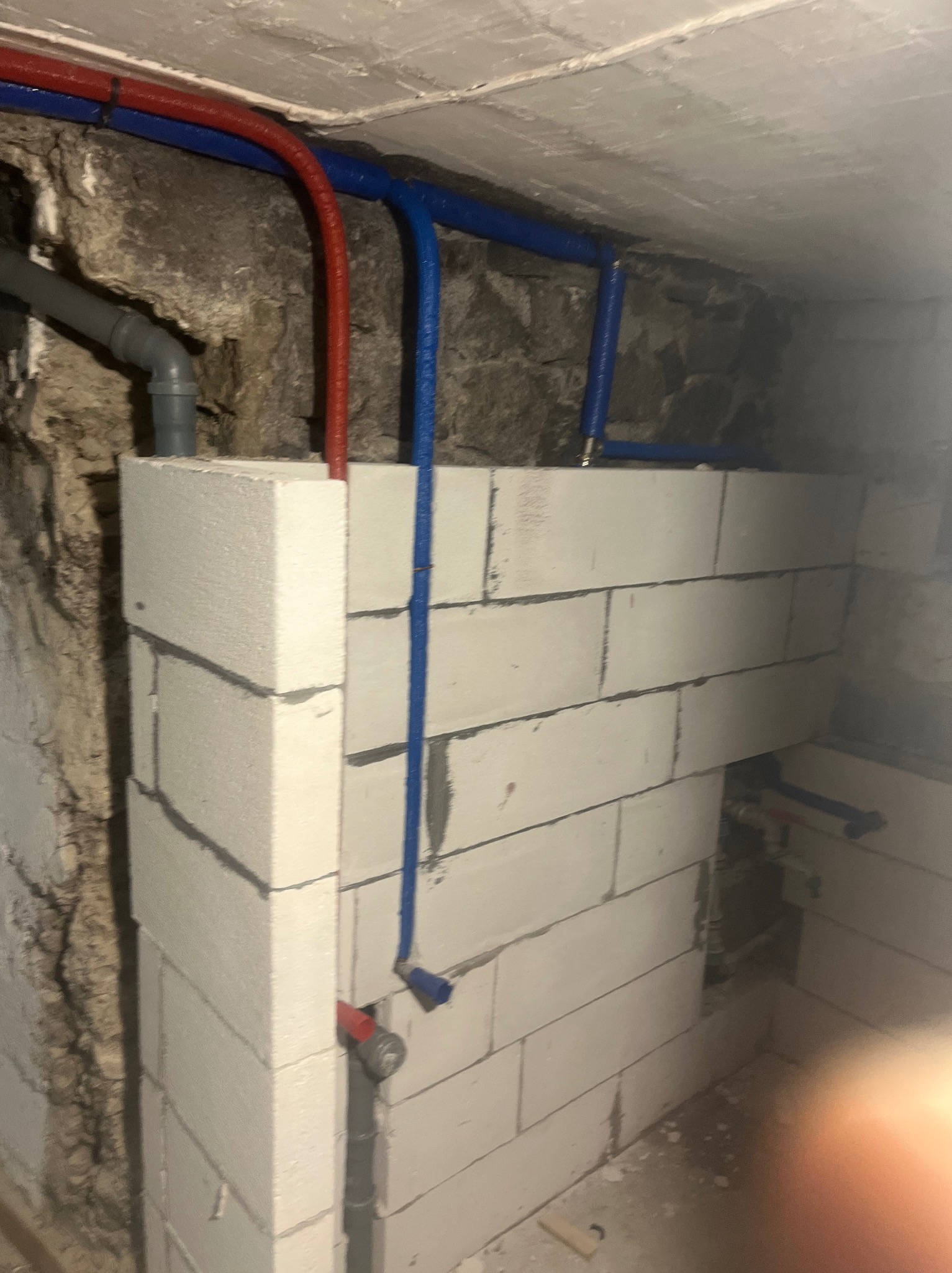 Instalacja wodna z rurami w kolorze niebieskim i czerwonym, zamontowana na ścianie z białych bloczków. Widoczne fragmenty starej, kamiennej ściany.