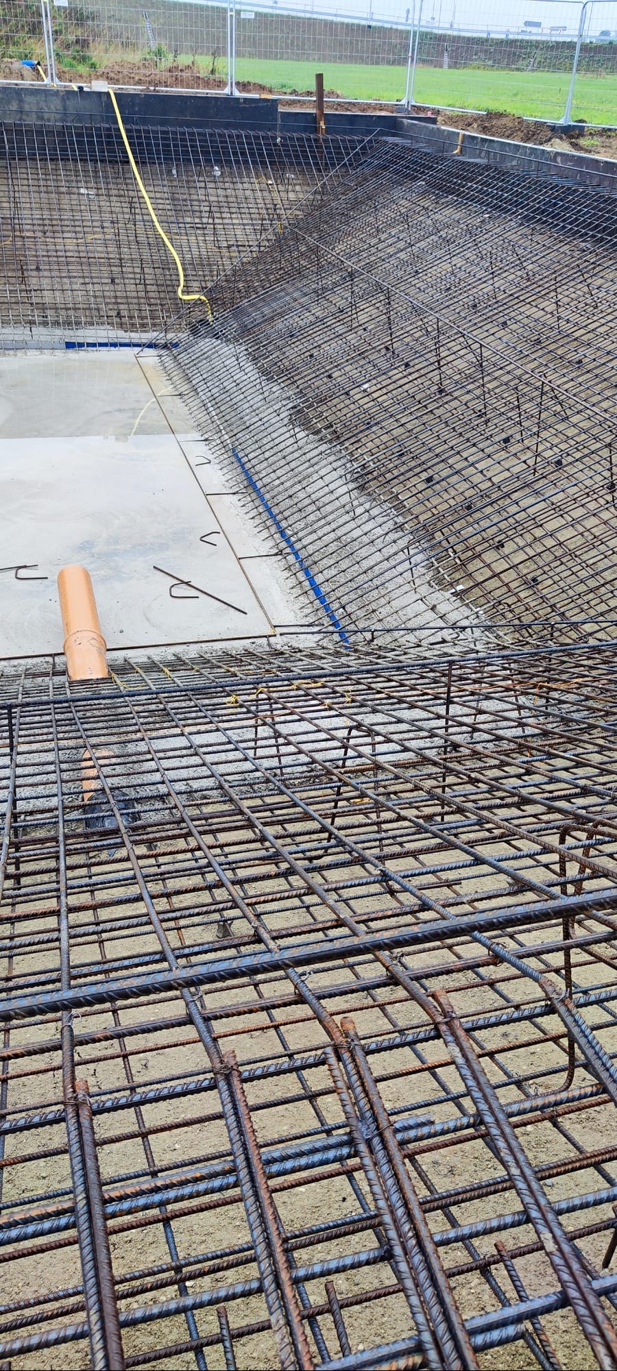 Zbrojenie fundamentów pod budynek z widoczną siatką stalową, rurą kanalizacyjną i żółtym kablem. Prace przygotowawcze do wylewania betonu.