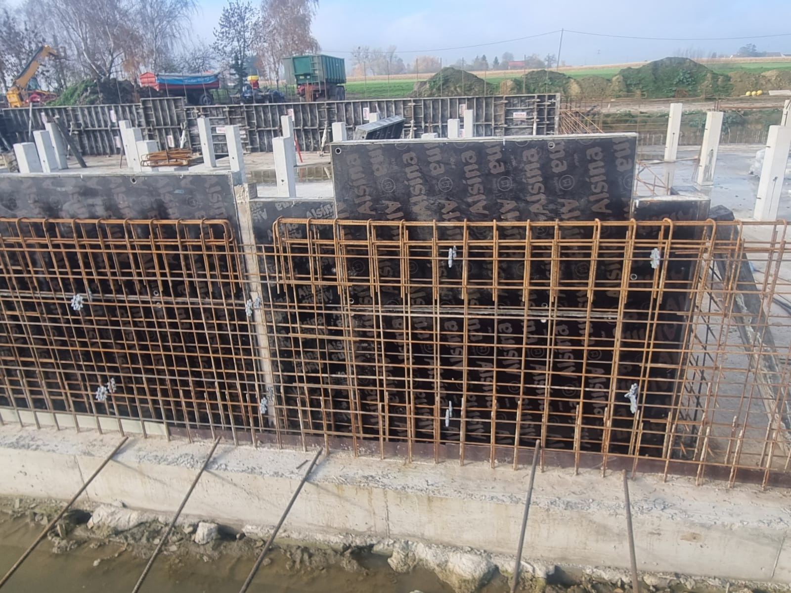 Zbrojenie fundamentów z deskowaniem i siatką stalową na budowie. Widoczne elementy konstrukcyjne i przygotowanie do zalewania betonem.