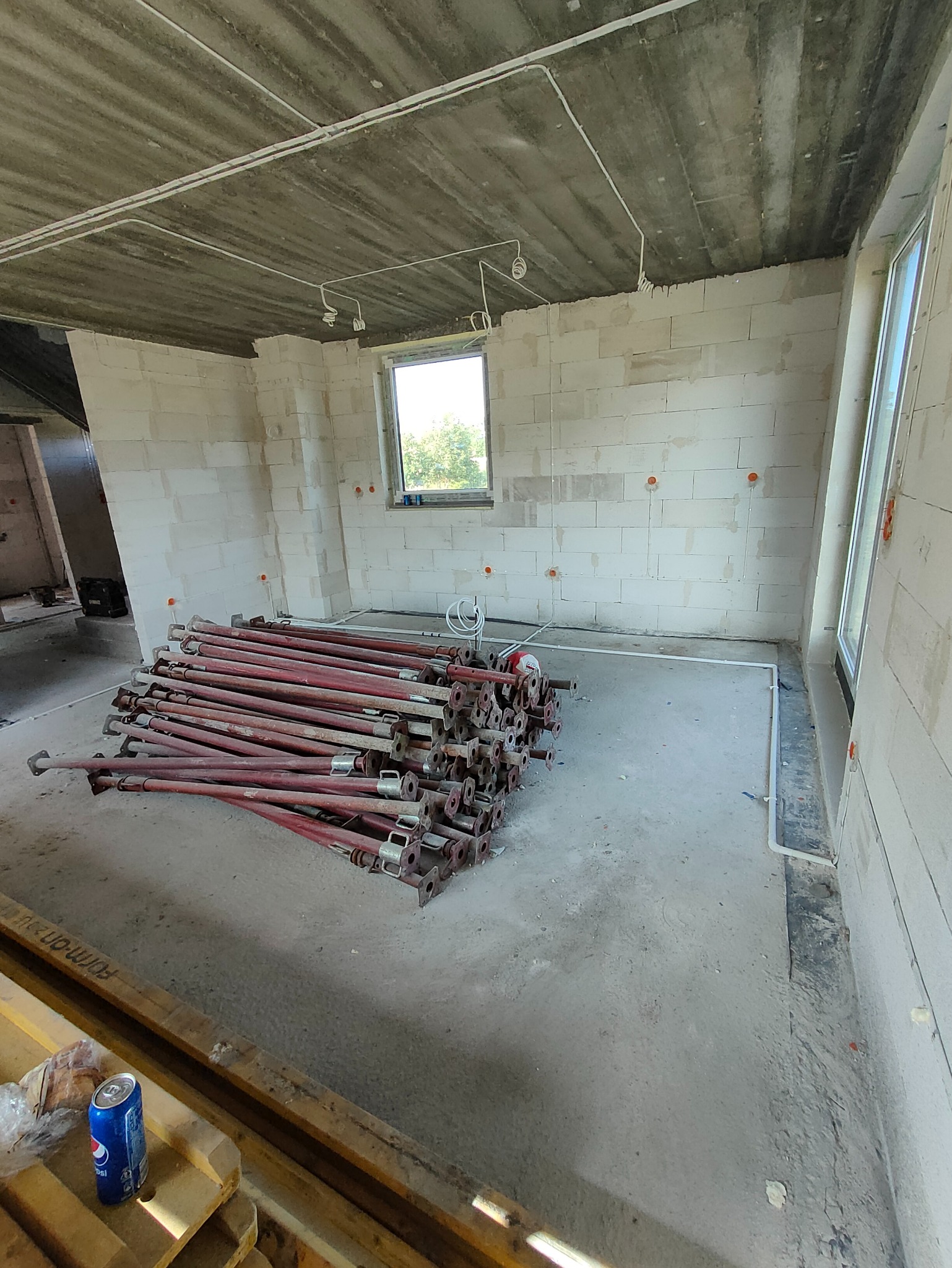 Surowy stan wnętrza z instalacją elektryczną pod sufitem, stertą podpór budowlanych i puszkami elektrycznymi w ścianach z betonu komórkowego.