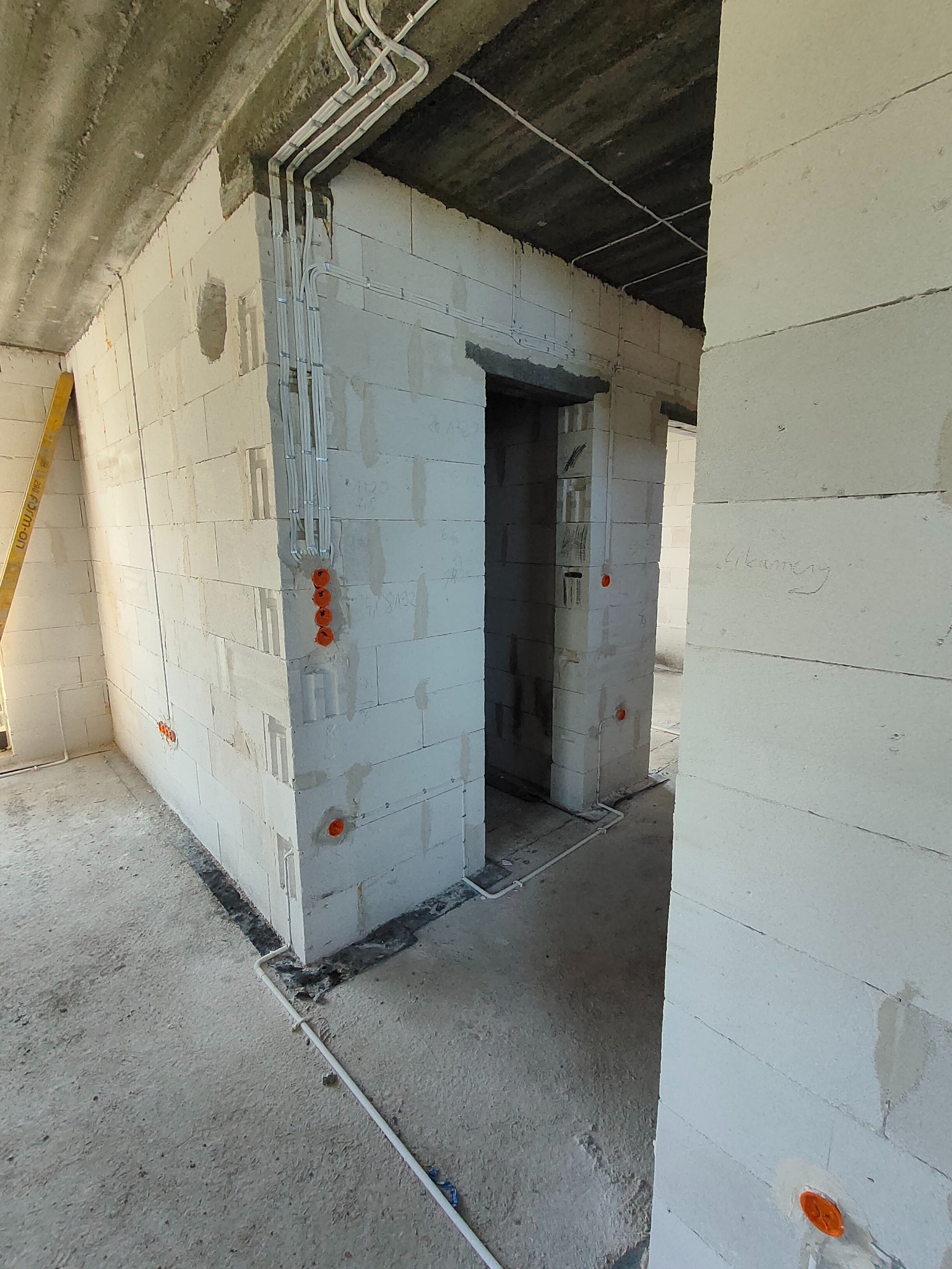 Wnętrze w trakcie instalacji elektrycznej: kable w peszlach prowadzone po ścianach z betonu komórkowego, pomarańczowe puszki elektryczne. Widoczny surowy stan wykończenia.