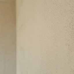 Jakub Porzyczek - Ściana po nałożeniu tynku w jasnym odcieniu beżu, widoczna faktura. Ujęcie z bliska, ukazujące gładką powierzchnię i narożnik ściany.