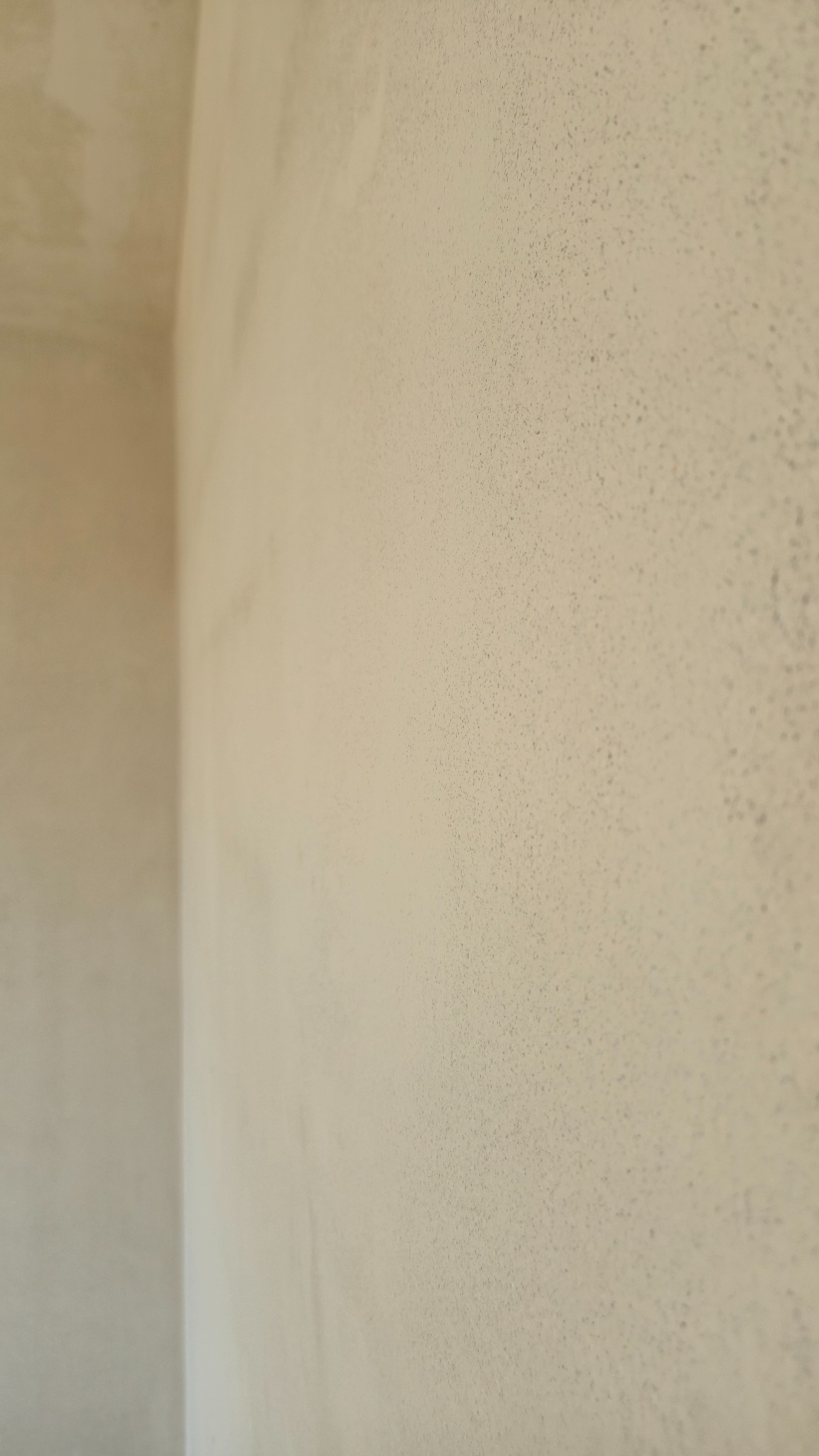 Ściana po nałożeniu tynku w jasnym odcieniu beżu, widoczna faktura. Ujęcie z bliska, ukazujące gładką powierzchnię i narożnik ściany.