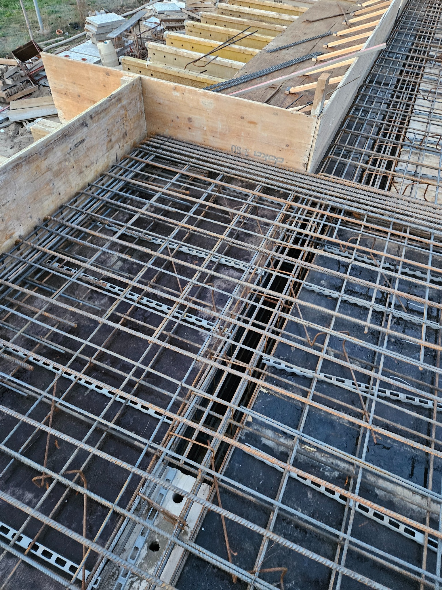 Zbrojenie stropu z drewnianym szalunkiem, widoczne stalowe pręty i elementy dystansowe. Ujęcie z góry, ukazujące etap budowy domu jednorodzinnego.