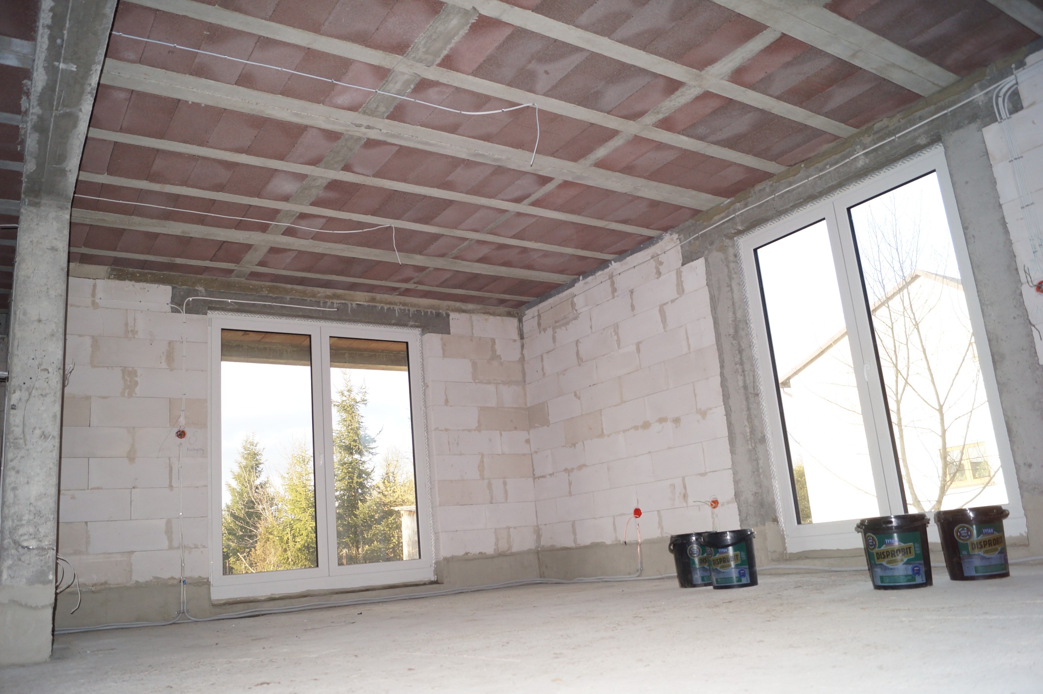 Surowy stan wnętrza z oknami i stropem Teriva w Mińsku Mazowieckim. Widoczne puszki z farbą, ściany z bloczków i instalacje elektryczne.