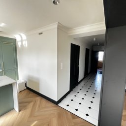 Katruk Technologies - Korytarz po remoncie: parkiet w jodełkę, biało-czarna podłoga w romby, czarne drzwi i listwy przypodłogowe. Widoczna część zielonej zabudowy kuchennej.