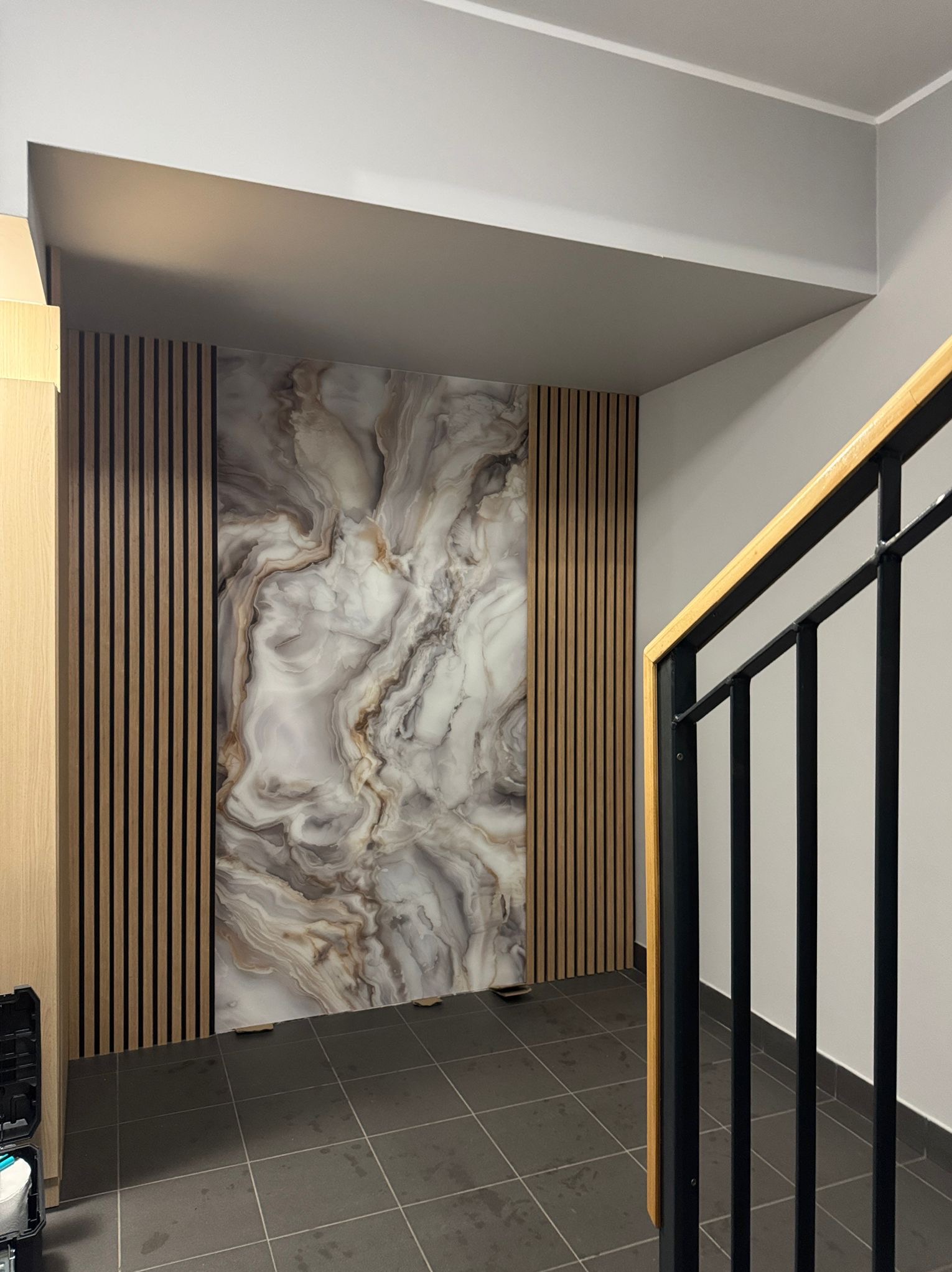 Nowoczesna aranżacja ściany z panelami drewnianymi i marmurową płytą w klatce schodowej. Minimalistyczny design z akcentem na naturalne materiały i tekstury.