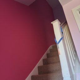 DM Renovations - Schody w domu po malowaniu ścian na intensywny róż i fiolet. Widoczne schody z wykładziną i biała balustrada z niebieską smyczą.