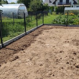 KP NOVA BUD Krzysztof Pisarek - Przygotowany teren pod uprawę z ogrodzeniem panelowym na betonowej podmurówce. W tle szklarnia, dom i błękitne niebo z chmurami.