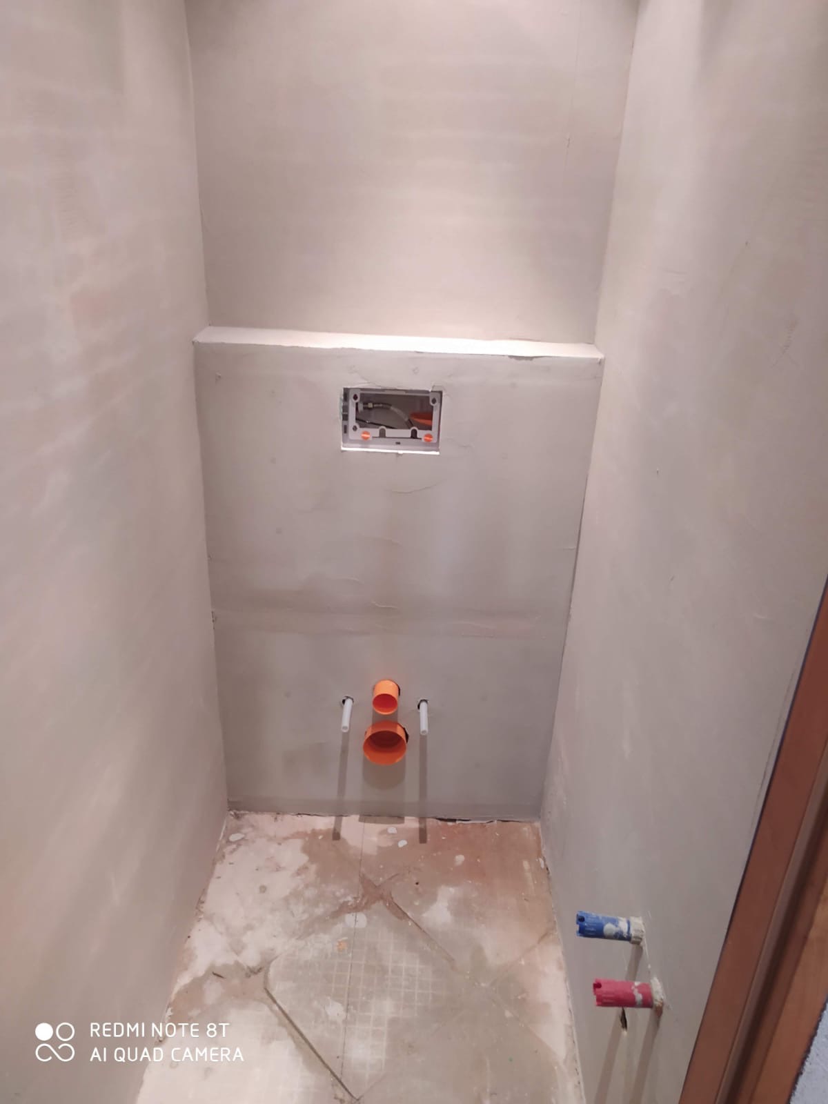 Surowa łazienka w trakcie prac: ściany po gładzi, widoczne instalacje wodne i stelaż podtynkowy WC. Podłoga przygotowana do dalszych prac wykończeniowych.