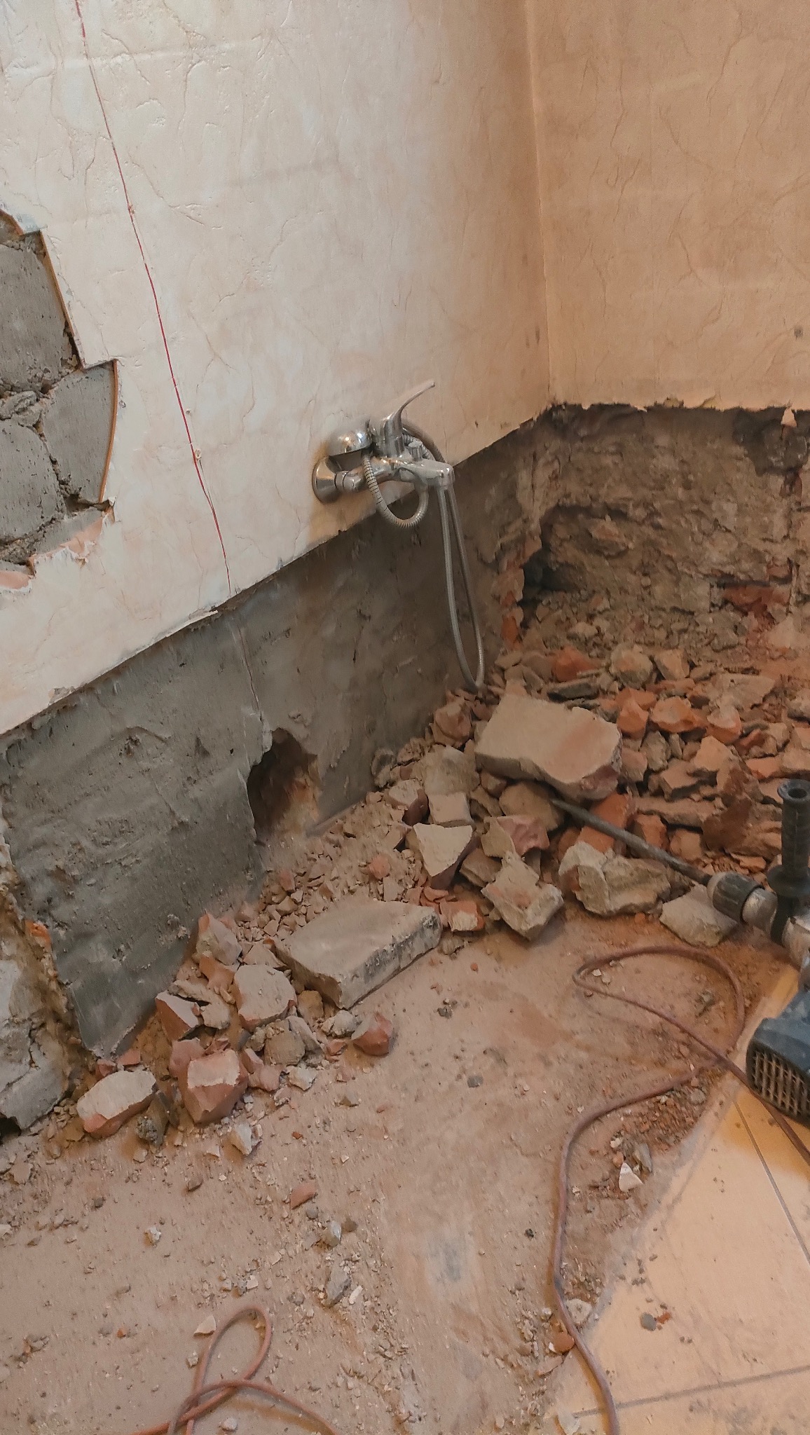 Demontaż płytek w łazience, widoczne fragmenty gruzu i odsłonięta instalacja wodna. Przygotowanie do remontu, widok na usunięte fragmenty ściany i podłogi.