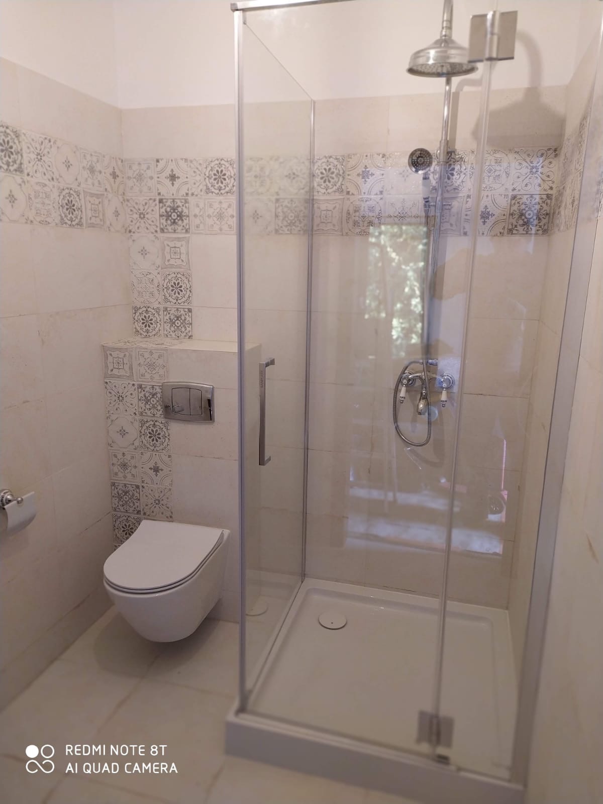 Nowoczesna łazienka z kabiną prysznicową, wiszącą toaletą i dekoracyjnymi płytkami. Widok na wnętrze kabiny przez przezroczyste szkło.