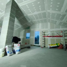 Maciej Arent - Poddasza i wykończenia - Poddasze w trakcie wykańczania: zamontowane płyty gipsowe na skosach i ścianach, widoczne szpachlowane łączenia, rusztowanie, worki z zaprawą. Prace wykończeniowe.