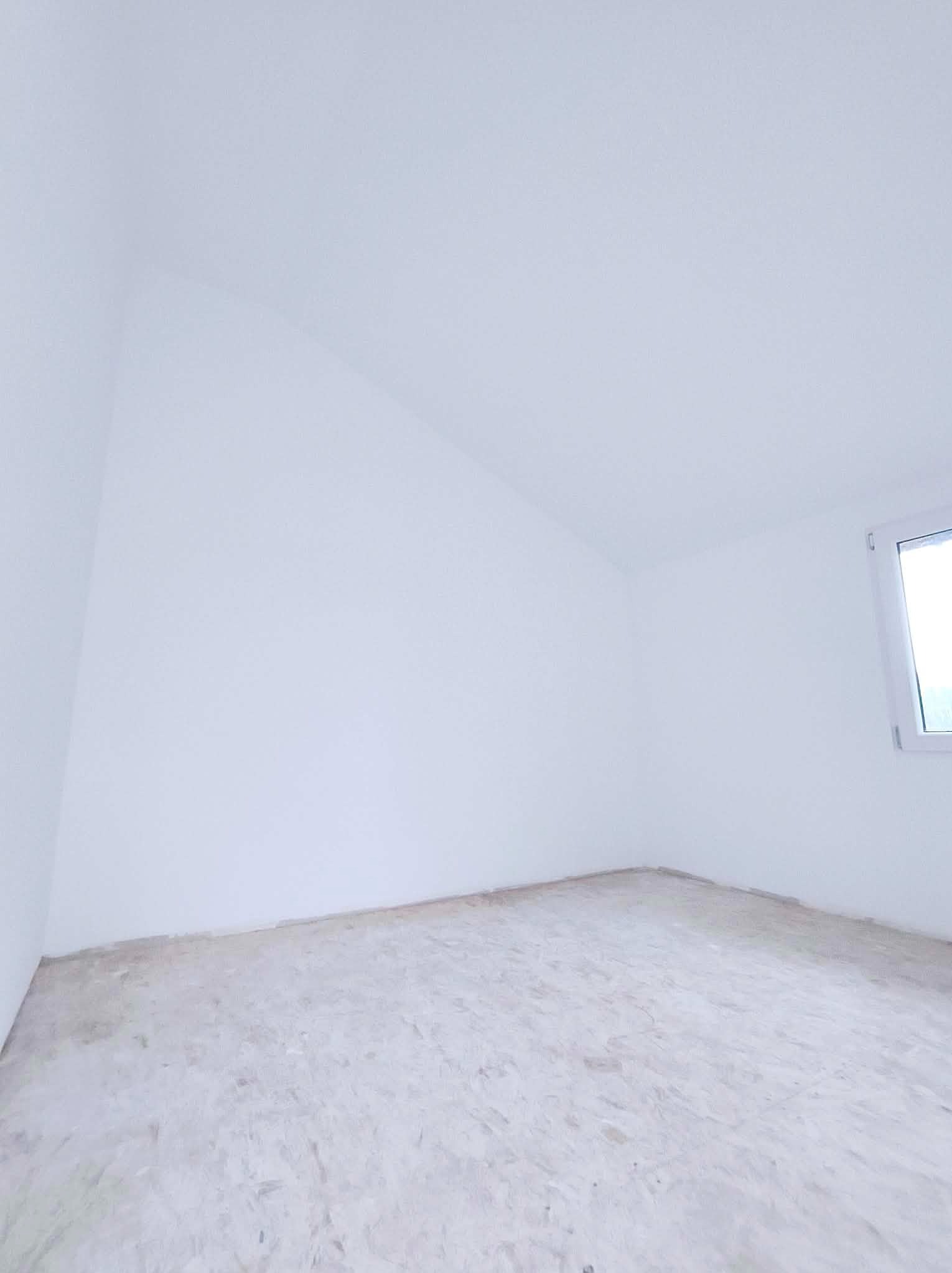 Białe, puste wnętrze pokoju z oknem, przygotowane do prac wykończeniowych. Widoczna surowa podłoga i świeżo pomalowane ściany, gotowe do dalszych etapów remontu.