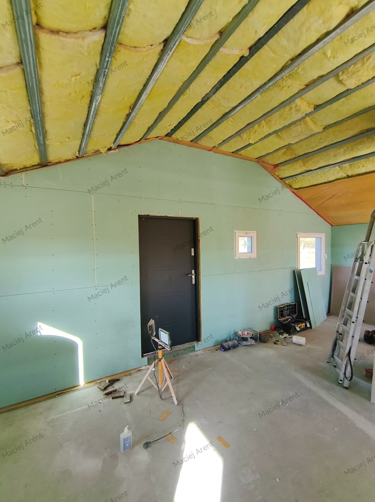 Poddasze z ociepleniem z wełny mineralnej i zamontowanymi płytami gipsowo-kartonowymi. Widoczne narzędzia i drabina. Prace w toku, surowy stan.