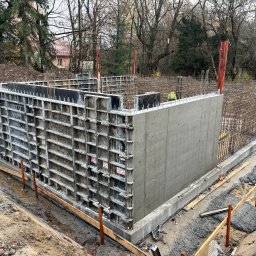 Budmar - Wylany fundament z szalunkiem systemowym i zbrojeniem, widok z góry. Etap budowy domu, teren budowy z drzewami w tle. Prace fundamentowe w toku.