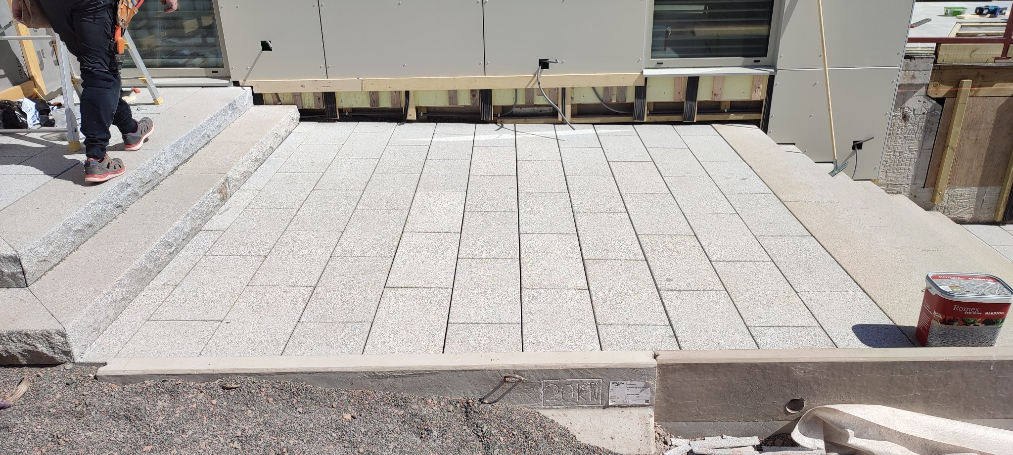 Jasnoszara kostka granitowa ułożona na podjeździe, widok z góry, z boku widoczny fragment schodów i puszka z preparatem do spoinowania Romex Hardfog.