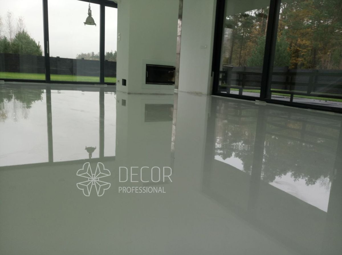 Błyszcząca, jasnoszara posadzka w nowoczesnym wnętrzu z dużymi oknami. Widoczne odbicia otoczenia w gładkiej powierzchni. Minimalistyczny design z kominkiem w tle.